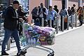 Ein Mann schiebt einen randvollen Einkaufswagen an einer Schlange von Menschen vorbei, die auf Einlass in einen Supermarkt warten. Aufgrund der Coronavirus-Pandemie kaufen viele Menschen sehr viele Lebensmittel auf Vorrat.&nbsp;