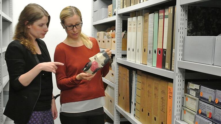 Die wissenschaftliche Leiterin Daniela Sandner (links) und ihre Mitarbeiterin Romana Wahner (rechts) im Depot des Deutschen Fastnachtmuseums in Kitzingen mit einer alten Rhöner Maske. Die wissenschaftliche Leiterin Daniela Sandner (links) und ihre Mitarbeiterin Romana Wahner (rechts) im Depot des Deutschen Fastnachtmuseums in Kitzingen mit einer alten Rhöner Maske. 