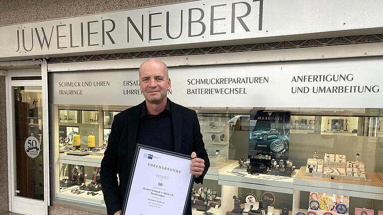 Stefan Neubert mit der Ehren-Urkunde der IHK zum 50-jährigen Bestehen vor seinem Schmuckgeschäft. - Stefan Neubert mit der Ehren-Urkunde der IHK zum 50-jährigen Bestehen vor seinem Schmuckgeschäft. Stefan Neubert mit der Ehren-Urkunde der IHK zum 50-jährigen Bestehen vor seinem Schmuckgeschäft. - Stefan Neubert mit der Ehren-Urkunde der IHK zum 50-jährigen Bestehen vor seinem Schmuckgeschäft.