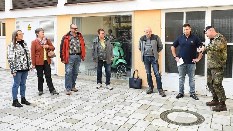 Kai Sell (in Uniform) erklärt den Vertretern der Streutal-Allianz die Konzeption des Doku-Zentrums und was das vom KFG gestaltete Schaufenster darstellt. 3.&nbsp; von links Martin Link, der 1. Vorsitzende der Streutal-Allianz; rechts neben ihm Brigitte Proß vom Verein 'Aktives Mellrichstadt'. Links neben Sell: Lucas Amberg und Markus Budde vom KFG.