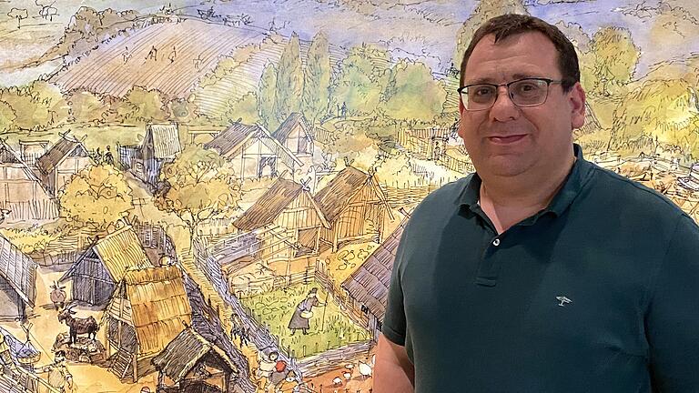 Markus Mergenthaler, Leiter des Knauf-Museums in Iphofen und Kurator der Ausstellung 'Als Franken fränkisch wurde' (verlängert bis 7. November 2021) steht vor einer historisierenden Ansicht eines frühmittelalterliches Dorfes&nbsp; (Zeichnung Wladimir Petrichev, Würzburg).