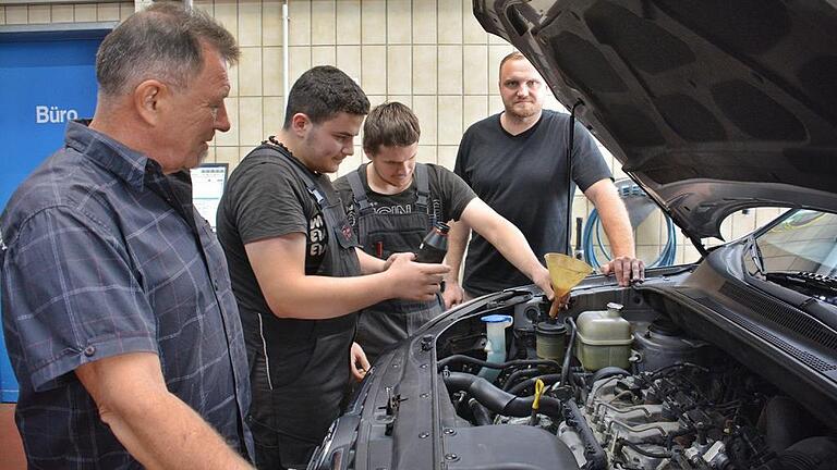 Zufrieden mit ihrem syrischen Lehrling: Karl-Otto Behrmann (links) und sein Sohn Dominic (hinten rechts) beobachten Amjad, der unter Anleitung des Gesellen Domenic Hültner an einem Fahrzeug Servo-Öl nachfüllt.