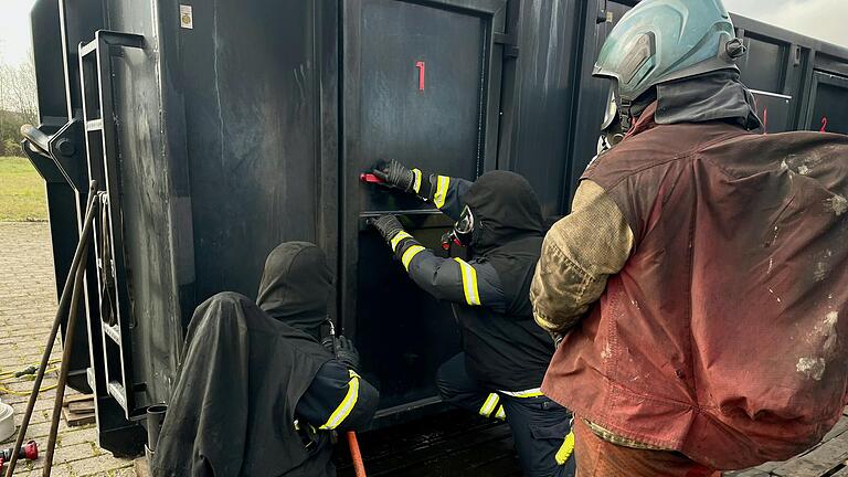 Vorsichtig öffnet ein Feuerwehrmann die Stahltür des Brandcontainer. Sein Kamerad sichert mit einem C-Schlauch.