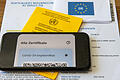 Ein Impfpass und ein Smartphone, auf dem die App CovPass läuft, liegen auf einem Impfzertifikat, das von einer Apotheke ausgestellt wurde. (Symbolfoto)