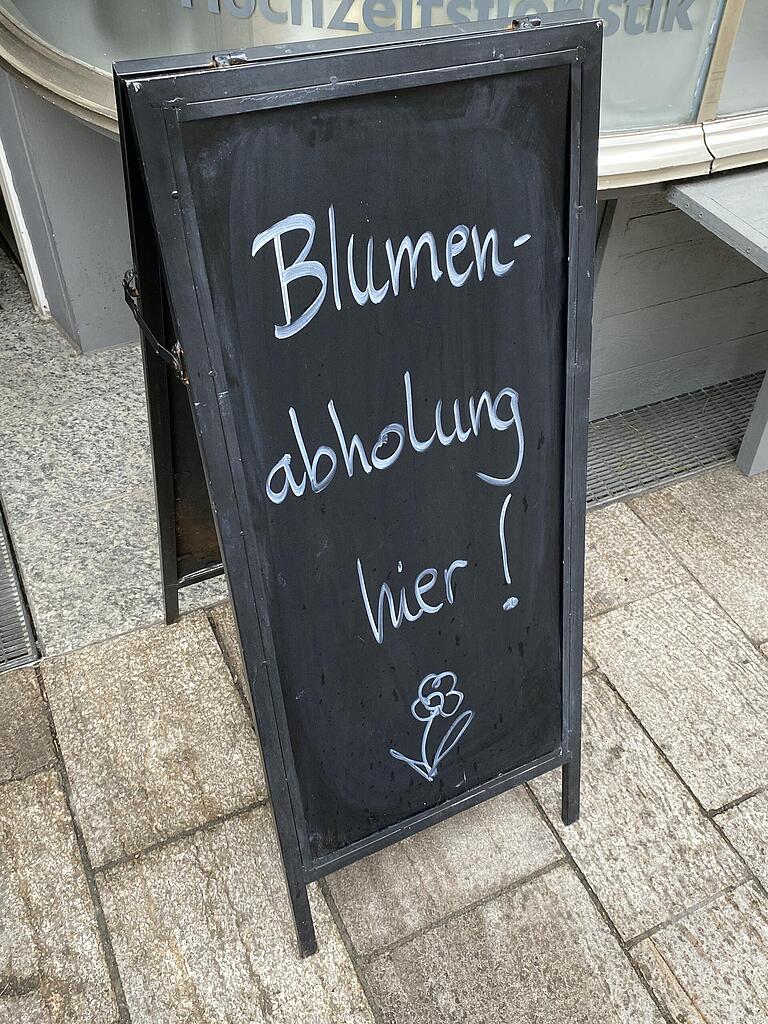 Eine Tafel wirbt vor dem Laden für eine Abholung des Blumenschmucks.