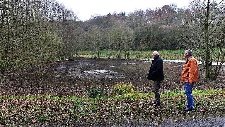 Trocken sieht der Teich aus, nachdem ihm das Wasser entzogen worden war. Doch der Schein trügt: Der Boden ist schlammig-morastig und damit gefährlich für jeden, der hineingerät. Die hellen Flecken in der Mitte sind tote Fische, wie Karlheinz Herda (rechts) und Wolfgang Klemm berichten. Trocken sieht der Teich aus, nachdem ihm das Wasser entzogen worden war. Doch der Schein trügt: Der Boden ist schlammig-morastig und damit gefährlich für jeden, der hineingerät. Die hellen Flecken in der Mitte sind tote Fische, wie Karlheinz Herda (rechts) und Wolfgang Klemm berichten.