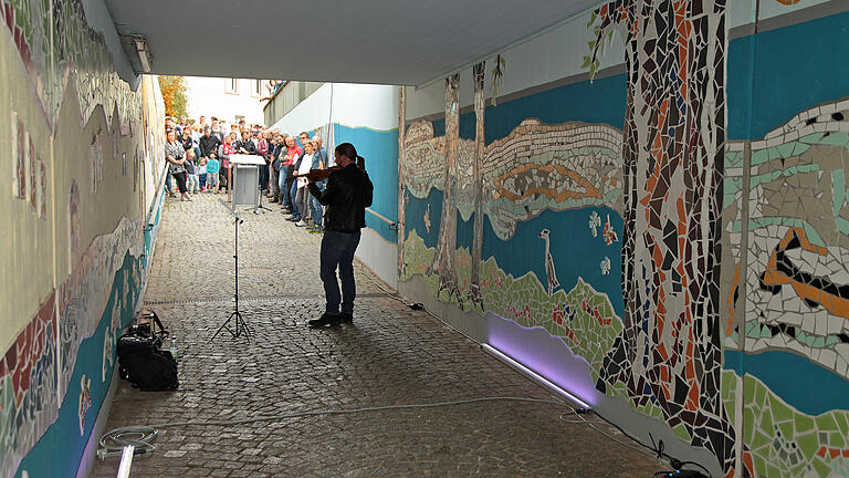 Als Gegenpol zur Silhouette des Ortes (links) entstand durch die Darstellung des Mainufers mit seinen Tieren und majestätischen Pappeln in der ehemals tristen Bahnunterführung in Thüngersheim ein filigranes Kunstwerk aus Fließen-Mosaik zu dem Geiger Oliver Szykulski bei der Übergabe virtuos seinen Beitrag leistete. Foto: Herbert Ehehalt