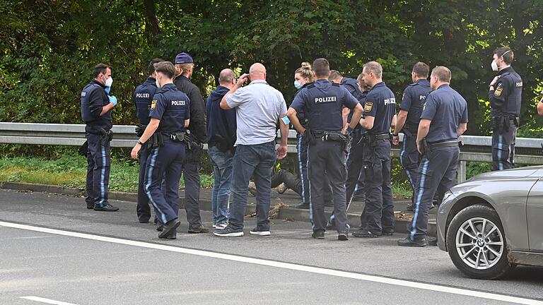 Kurz nach dem Raubüberfall im Ochsenfurter Stadtteil Hohestadt (Lkr. Würzburg) wurde der mutmaßliche Täter an der Staatsstraße nach Tückelhausen festgenommen. Hier sitzt er am Bordstein zwischen den Polizistinnen und Polizisten und wartet auf seinen Abtransport.