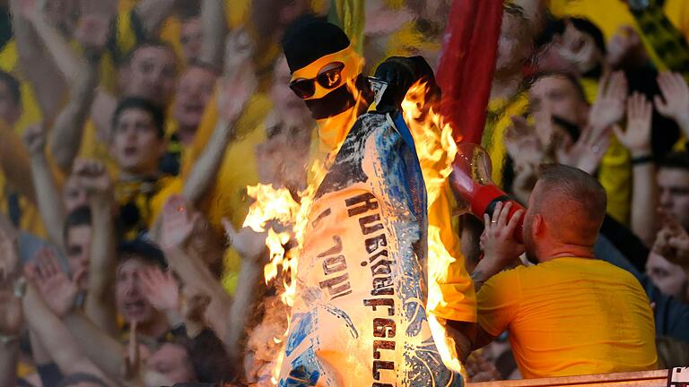 Auch das gehört zum Auftreten der Ultras in den Stadien: das Verbrennen 'gegnerischer' Fan-Utensilien, wie hier durch einen mit einer Sturmhaube vermummten&nbsp; Dortmunder im 2019er Derby gegen Schalke 04.