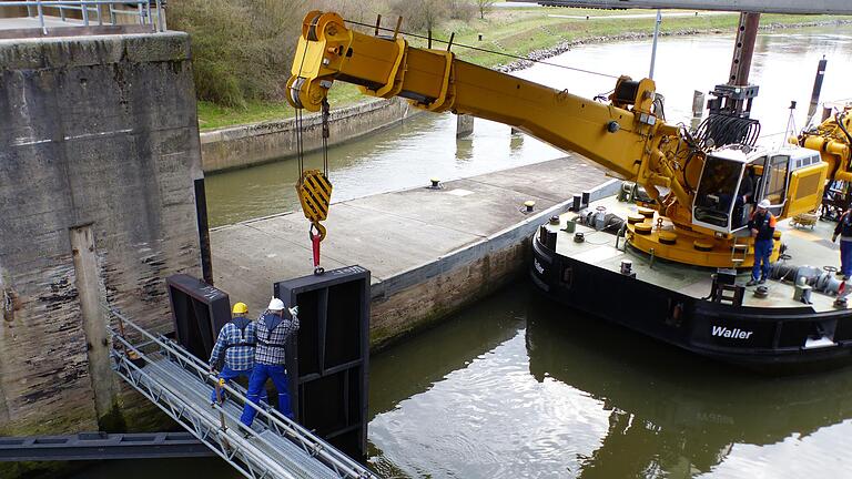 Am Untertor der Schleuse Gerlachshausen ist ein Schwimmkran im Einsatz, der ebenfalls Verschlussplatten einsetzt. Knapp darüber verläuft die Straße nach Sommerach. Am Untertor der Schleuse Gerlachshausen ist ein Schwimmkran im Einsatz, der ebenfalls Verschlussplatten einsetzt. Knapp darüber verläuft die Straße nach Sommerach.