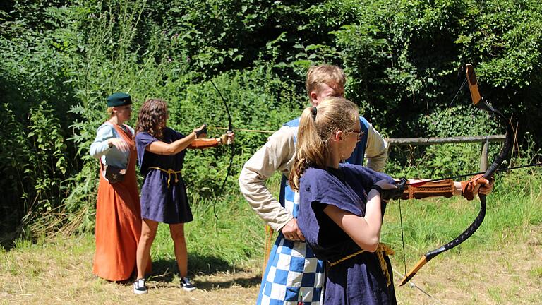 Lady Doria von Sievershof (hinten l.) und Sir Jonas von Wolfenstein (2. von r.) üben mit ihren jungen Besuchern das Bogenschießen im Burggraben, das feindlich Gesinnte auf Distanz halten soll.       -  Lady Doria von Sievershof (hinten l.) und Sir Jonas von Wolfenstein (2. von r.) üben mit ihren jungen Besuchern das Bogenschießen im Burggraben, das feindlich Gesinnte auf Distanz halten soll.