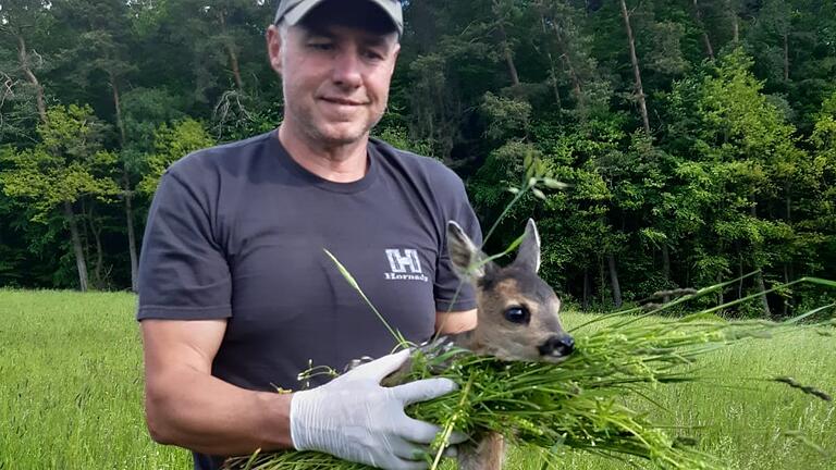 Matthias Reith trägt ein Rehkitz aus der Wiese.