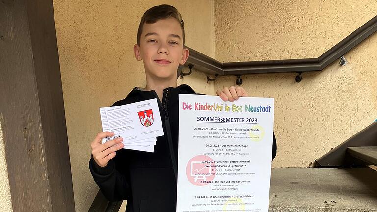 Stolz präsentiert der KinderUni-Student Eric Tapken das neue Plakat und die neuen Ausweise, die ab sofort in der Geschäftsstelle der Vhs Bad Neustadt erhältlich sind.