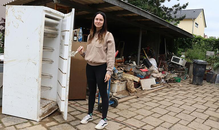 Laura Scherer steht vor einem Kühlschrank und anderen Habseligkeiten, die noch immer die Spuren des nächtlichen Hochwassers tragen.