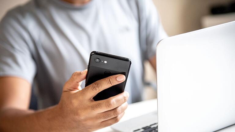 Junger Mann mit Smartphone und Laptop       -  Beim Onlinebanking gilt: Lieber etwas aufmerksamer sein, als das Nachsehen zu haben.