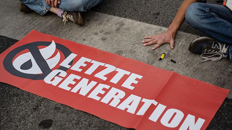 Letzte Generation.jpeg       -  Ein Aktivist der Gruppe Letzte Generation, der seine Hand selbst auf der Straße festgeklebt hat, blockiert eine Kreuzung in Göttingen (Archivbild).