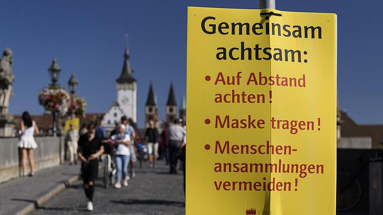 Große Schilder verweisen auf der Alten Mainbrücke in Würzburg auf die geltenden Coronaregeln.