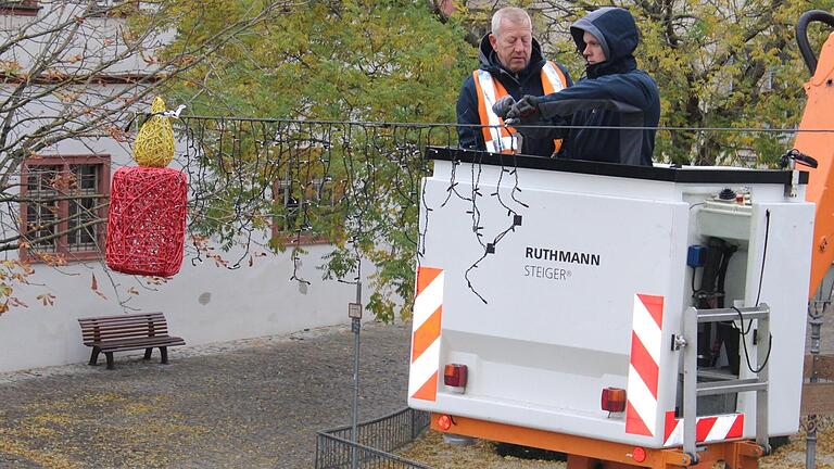 Mitarbeiter der Licht-, Kraft- und Wasserwerke befestigen die neue Weihnachtsbeleuchtung über den Straßen der Kitzinger Altstadt.