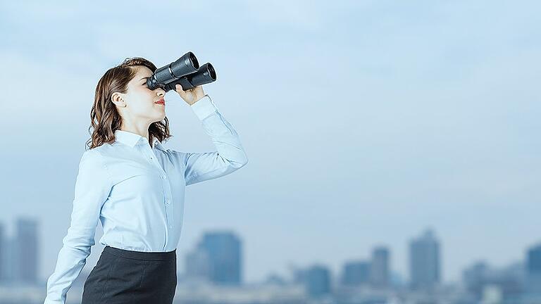 Young businesswoman using binoculars in front of the city.       -  In die Ferne blicken, um dort Maschinen und Anlagen per Klick zu warten: Das machen mittlerweile einige Firmen in Mainfranken.