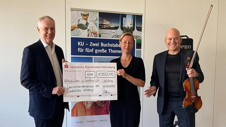 Bernd Fröhlich (Vorsitzender Stiftungsvorstand der Sparkassenstiftung, links) überreicht Eva von Vietinghoff-Scheel (Vorständin Kommunalunternehmen) eine Spende in Höhe von 1000 Euro für die Veranstaltungsreihe Kulturbrücken, im aktuellen Programm mit Künstler Florian Meierott (rechts).