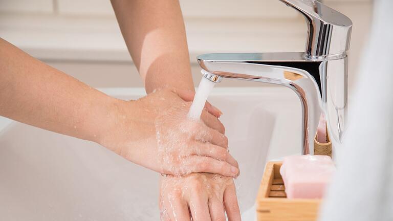 Eine Frau lässt sich Wasser über die Hände laufen - Kleine Selbstfürsorge-Maßnahmen, wie kaltes Wasser über die Hände, können Stressmomente entschärfen. Eine Frau lässt sich Wasser über die Hände laufen - Kleine Selbstfürsorge-Maßnahmen, wie kaltes Wasser über die Hände, können Stressmomente entschärfen.