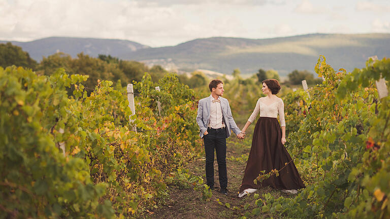 Romantic and stylish caucasian couple standing in the beautiful vineyard       -  Kombiniert mit Tradition und Genuss, gibt es keine engere Verbundenheit zur Heimat als die Hochzeitsfeier auf einem Weingut