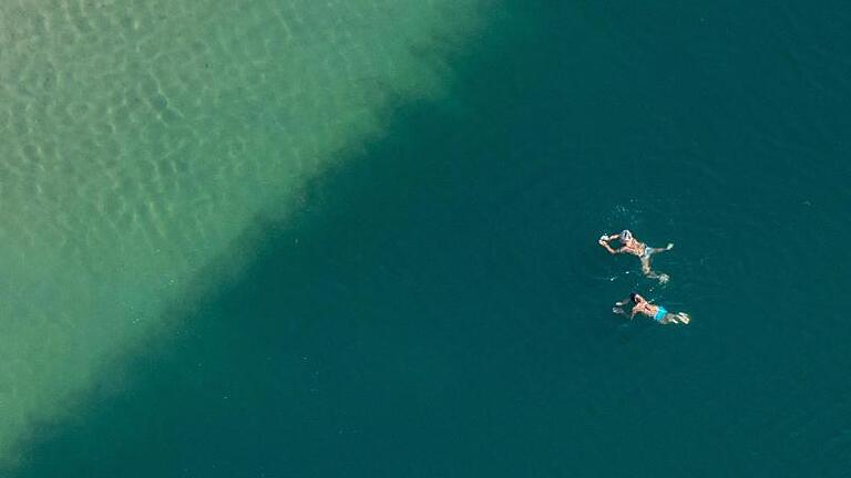 Badegäste schwimmen in einem See. Foto: Armin Weigel       -  Italien glänzt nicht nur bei Badegästen mit seinen Seen.