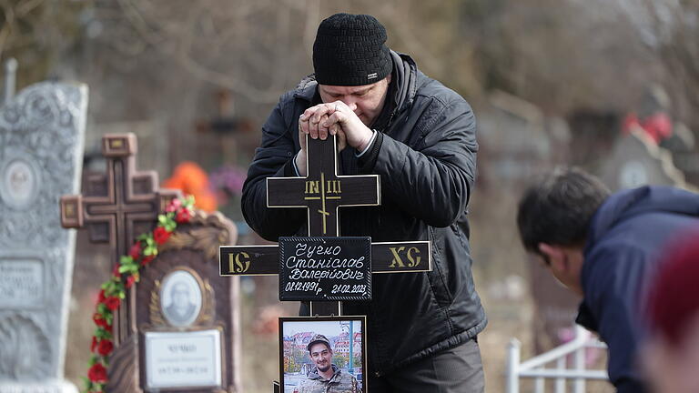 Ukraine - Krieg - Saporischschja       -  Ein Mann legt ein Kreuz auf das Grab eines ukrainischen Soldaten, der im Kampf um die Stadt Bachmut im Osten der Ukraine getötet wurde.