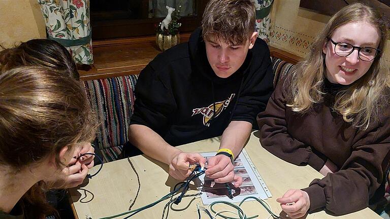 Jugendliche beim Abendprogramm auf der Foto Berghütte: Knüpfen von Paracord-Armbändern (Leander Martin aus Oberbach (Mitte) und Skicampleiterin Lysann Knopp aus Sailauf (rechts). - Jugendliche beim Abendprogramm auf der Foto Berghütte: Knüpfen von Paracord-Armbändern (Leander Martin aus Oberbach (Mitte) und Skicampleiterin Lysann Knopp aus Sailauf (rechts). Jugendliche beim Abendprogramm auf der Foto Berghütte: Knüpfen von Paracord-Armbändern (Leander Martin aus Oberbach (Mitte) und Skicampleiterin Lysann Knopp aus Sailauf (rechts). - Jugendliche beim Abendprogramm auf der Foto Berghütte: Knüpfen von Paracord-Armbändern (Leander Martin aus Oberbach (Mitte) und Skicampleiterin Lysann Knopp aus Sailauf (rechts).