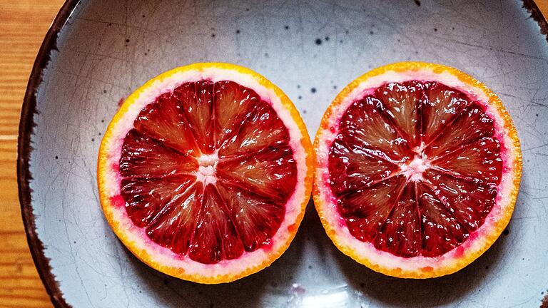 Aufgeschnittene Blutorange auf einem Teller       -  Blutorangen schmecken herb-würzig bis süß-säuerlich und passen gut in einen Obstsalat, Kuchen oder Desserts.