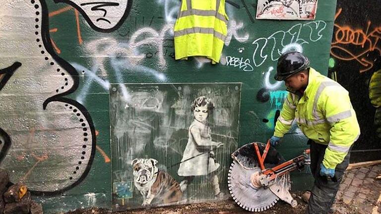 Ein Bauarbeiter in der englischen Stadt Bristol schickt sich an, das teilweise übersprühte Graffito von Jamie Paul Scanlon aus der Wand des Abrisshauses zu schneiden.