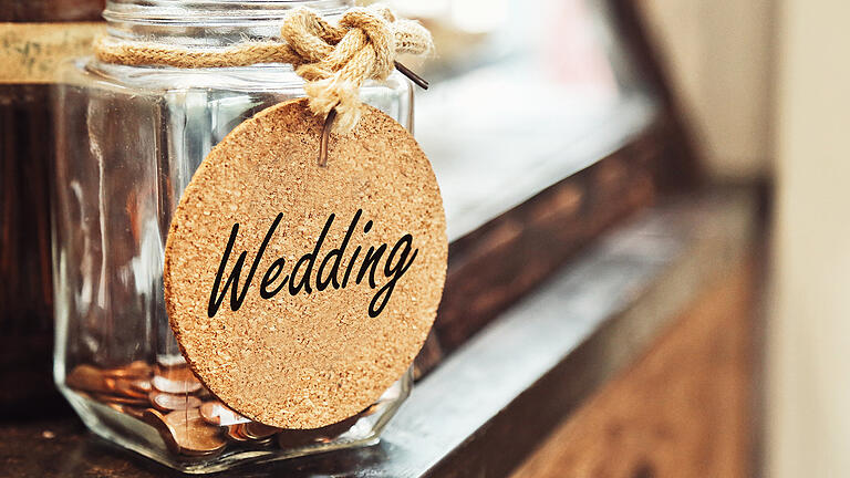 Vintage retro glass jar with hemp rope tie wedding tag and few coins inside on wood counter concept of saving money for wedding       -  Manche haben nur ein kleines Budget zur Verfügung. Andere können Summen ausgeben, für die man einen gehobenen Mittelklassewagen bekommt. Doch wie viel Geld müssen Paare einplanen?