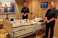 Zwei Saluto-Care-Pfleger in eleganter schwarzer Arbeitskleidung am Bett einer Penthaus-Suite.       -  Zwei Saluto-Care-Pfleger in eleganter schwarzer Arbeitskleidung am Bett einer Penthaus-Suite.