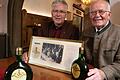 Der langjährige Bürgerspital-Weingutsleiter Rudolf Frieß (rechts) mit seinem Nachfolger Robert Haller&nbsp; im Jahr 2015. Im Vordergrund zwei Flaschen des Weins für das Essen mit der Queen 1965. Das Foto im goldenen Rahmen zeigt die Queen beim Essen auf Schloss Charlottenburg am 27. Mai 1965. Mit eingerahmt sind auch das Etikett des Bürgerspital-Weins und die Speisekarte.