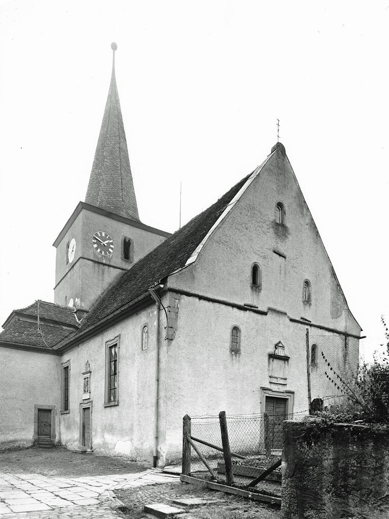 Auf dem Foto von 1967 ist die alte Burgwallbacher Kirche mit dem nördlichen Nebeneingang und dem Haupteingang auf der Westseite abgebildet. Der Erweiterung musste auch der ehemalige Schulgarten im Vordergrund weichen.