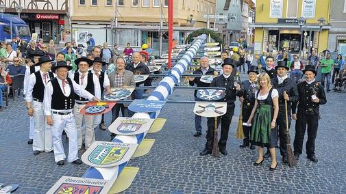 Der Zunftbaum steht: Jetzt beginnt die Marktplatz-Saison       -  (new)   Zum ersten Fest der Marktplatz-Saison lachte der Himmel. Stolz begleiteten die Zünfte ihren Wappenbaum zum Aufstellen. Zweite Bürgermeisterin Anne Zeisner (rechts vorne) bezeichnete das Symbol als Bekenntnis zur Handwerkerschaft und dankte allen, die zum Gelingen der Feier beitrugen: der Musikkapelle Brendlorenzen mit Dirigent Jürgen Weyer, der Rhöner Volkstanzgruppe, ohne die eine Zunftbaumaufstellung nicht denkbar sei, der Feuerwehr, die für das leibliche Wohl sorgte und dem städtischen Bauhof mit seinem Leiter Konrad Wehe fürs gekonnte Aufstellen. Jetzt können die Blicke wieder am weiß-blauen Stamm hinaufwandern - 19,85 Meter hoch. Auch Thomas Habermann, diesmal als Viertellandrat und Dreiviertel-Bürger von Bad Neustadt, freute sich über die Tradition, auf die Dietmar Rosshirt (links vorne), stellvertretender Kreishandwerksmeister und Obermeister der Bau-Innung, einging. Mit dem Dank für ein Jahr ohne größere Unfälle wolle der Zunftbaum auch die Bitte zum Ausdruck bringen: &bdquo;Gott segne das ehrbare Handwerk&ldquo;.