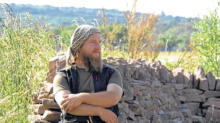 Mitten im Permakultur-Park bei Bischbrunn: Jonas Gampe an der Steinmauer, die sein Vater aufgeschichtet hat und die eine wichtige Funktion in der Wärmefalle für Gemüsebeete erfüllt &ndash; sie hält Wind ab und speichert Wärme.