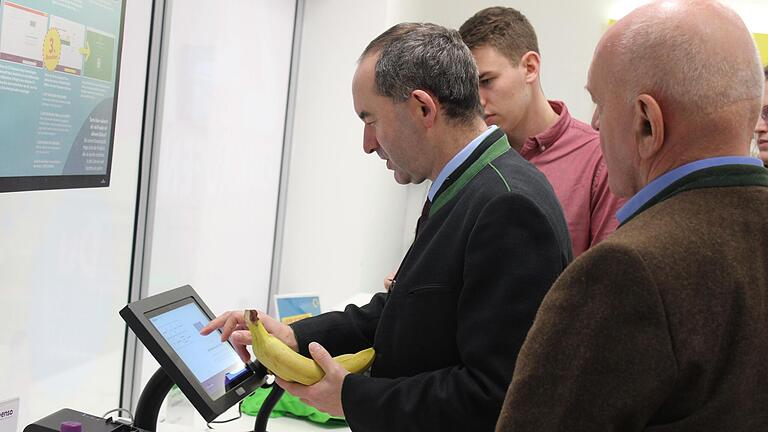 Wirtschaftsminister Hubert Aiwanger beim Bezahlen seiner Bananen, wobei er von Regionalleiter Ole Mehrtens und Landrat Thomas Habermann unterstützt wird. Wirtschaftsminister Hubert Aiwanger beim Bezahlen seiner Bananen, wobei er von Regionalleiter Ole Mehrtens und Landrat Thomas Habermann unterstützt wird.