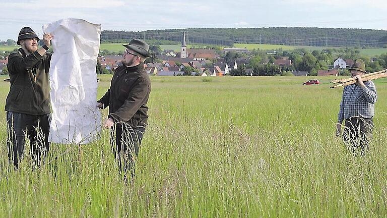 Ein simpler Trick: Einen Tag, bevor die Wiese gemäht wird, stellt Jagdpächter Hubert Helfrich (rechts) mit seinen Söhnen Fabian und Daniel (von links) solche Scheuchen auf. Diese sollen Rehgeiße dazu bringen, ihre Kitze woanders zu verstecken. Im Hintergrund ist Wiesenfeld.
