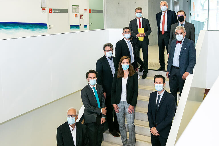 Gruppenbild mit Maske vor der gemeinsamen Pressekonferenz: (von unten im Uhrzeigersinn) Joachim Fuchs (Staatl. Bauamt Würzburg), Philip Rieger (Kaufmännischer Direktor Uniklinik), die persönliche OB-Mitarbeiterin Daniela Schuster, Prof. Peter Heuschmann (Leiter Institut für Klinische Epidemiologie und Biometrie), Prof. Stefan Störk (Leiter Klinische Forschung am DZHI und der STAAB-Studie), Wissenschaftsminister Bernd Sibler, Prof. Georg Ertl (Ärztlicher Direktor Uniklinik), Uni-Präsident Prof. Alfred Forchel, Prof. Matthias Frosch (Dekan Medizinische Fakultät) und DZHI-Sprecher Prof. Christoph Maack.