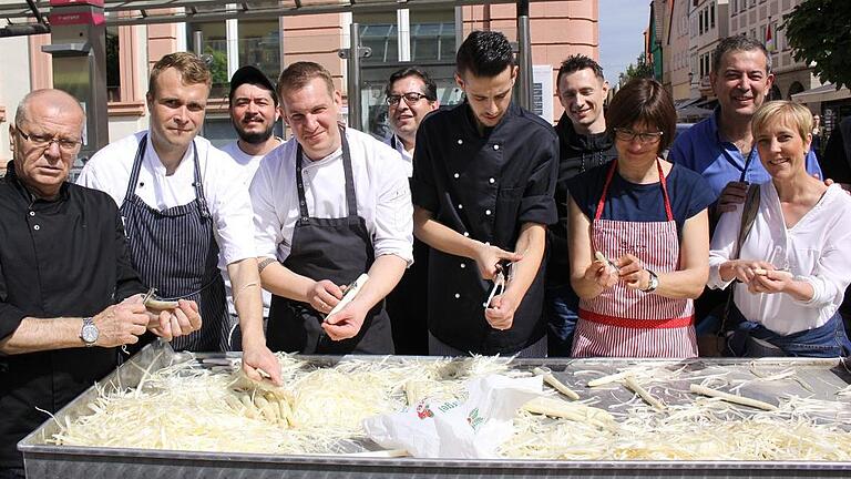 Sechs Zentner Spargel auf dem Marktplatz geschält       -  (ka)   Frischen Spargel kaufen und schälen lassen sowie bei flotter Musik Spargelcremesuppe und einen guten Schoppen genießen: All das hatte die Spargelschälaktion in Karlstadt am Samstag vor dem Muttertag zu bieten. Trotz eines Gewitterschauers zum Ende hin waren nach vier Stunden insgesamt sechs Zentner Spargel verkauft und geschält. Die freiwilligen Spenden für das Schälen kommen wieder der Musikschule Karlstadt zugute. Das Spargelschälen ist eine Gemeinschaftsaktion der Karlstadter Wirte und der Stadtmarketing-GmbH. Als prominente Schälerin griff diesmal Karlstadts dritte Bürgermeisterin Anja Baier zur Klinge. Außerdem schälten während der Aktion Manfred Schraud (Kegelstuben), Udo Vollert (Fehmelbauer), Dierk Fischer (Zeitlos), Francesco Zedda (Batzenärlle), Florian Josefs (Rose), Thomas Gsell (Steakhouse), Fabio Laurenzio (Mainpromenade), Birgitt Schaub (Bäckerei Schaub) sowie als Ehrenamtlicher Burkard Ehehalt. Den Weinverkauf organisierte Weinbau Frank. Weitere Helfer waren Dirk Bartstieber (Sparkasse), Volker Zimmer (Gonzos), Susanne Keller (Stadtmarketing-GmbH), Wolfgang Ries, Stavros Platakis und Peter Gsell. Die Suppe kochte und spendete Udo Vollert. Der Spargel stammte von den Spargelbauern Gold aus Karlburg und Schnackig aus Schönarts. Für die musikalische Untermalung sorgten anfangs das Percussion-, das Blechbläser- und das Saxofon-Ensemble der Musikschule Karlstadt im stetigen Wechsel sowie auch gemeinsam. In Hälfte zwei übernahm die Jazz-Combo.