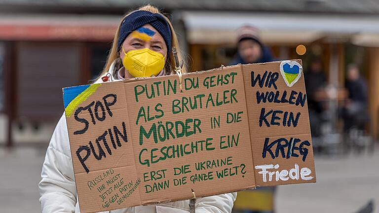 Ein Demonstratin in Würzburg hält ein Schild mit der Aufschrift 'Stop Putin'.