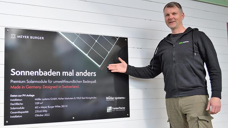 Frank Engler, Leiter Innendienst und für den Einkauf bei 'Müller systems' zuständig, neben einer Hinweistafel, die im Eingangsbereich über die neue PV-Anlage auf dem Dach der Frankentherme informiert.