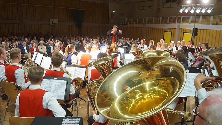 Der Blick über die Tuba von Oskar Schwab (rechts unter) über das Symphonische Blasorchester und dessen Dirigenten Manuel Scheuring in die vollbesetzte Mainschleifenhalle.
