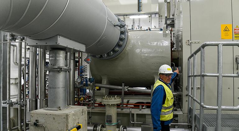 Das Herzstück in Rimpar: OGE-Projektleiter Jochen Kemper zeigt auf den runden Apparat, in dem das Gas neuen Druck für die Fernleitung bekommt. Rechts ist ein Teil des Gehäuses zu sehen, in dem eine Flugzeugturbine für den Antrieb des Verdichters sorgt.