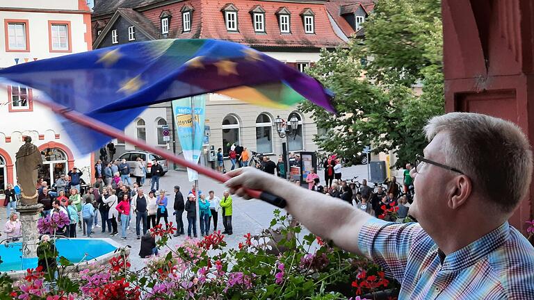 Der Volkacher Sebastian Kleinau schwenkte kurz vor Beginn der Stadtratssitzung die Europaflagge mit Regenbogen vom Rathausbalkon, um seine Solidarität mit Geflüchteten zu zeigen. Unten auf dem Marktplatz hatten sich Gegner des geplanten Flüchtlingsheims versammelt.