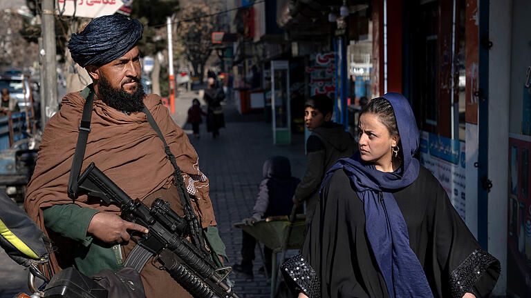 Frauenrechten in Afghanistan.jpeg       -  Ein Taliban-Kämpfer steht Wache, während eine Frau vorbeiläuft. Afghanistan erlebt unter den Taliban nach Angaben der Vereinten Nationen (UN) eine systematische Auslöschung von Frauenrechten.