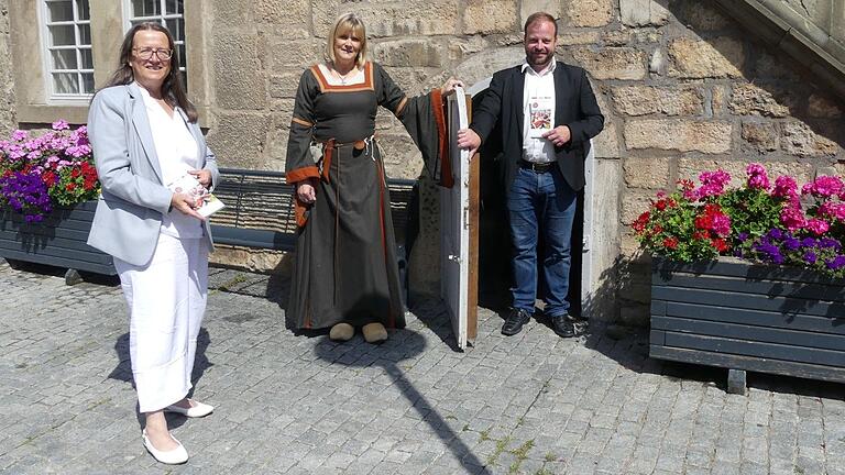 Von links nach rechts: Susanne Orf (Kommunalunternehmen Tourismus und Marketing), Susanne Zuber-Maisch (Stadtführerin in mittelalterlichem Gewand) und Bürgermeister Steffen Malzer mit dem neuen Flyer 'Historischer Stadtrundgang' vor einem der beiden 'Narrenhäuschen' am Rathaus in Ostheim. Von links nach rechts: Susanne Orf (Kommunalunternehmen Tourismus und Marketing), Susanne Zuber-Maisch (Stadtführerin in mittelalterlichem Gewand) und Bürgermeister Steffen Malzer mit dem neuen Flyer 'Historischer Stadtrundgang' vor einem der beiden 'Narrenhäuschen' am Rathaus in Ostheim.