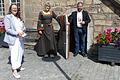 Von links nach rechts: Susanne Orf (Kommunalunternehmen Tourismus und Marketing), Susanne Zuber-Maisch (Stadtführerin in mittelalterlichem Gewand) und Bürgermeister Steffen Malzer mit dem neuen Flyer 'Historischer Stadtrundgang' vor einem der beiden 'Narrenhäuschen' am Rathaus in Ostheim.