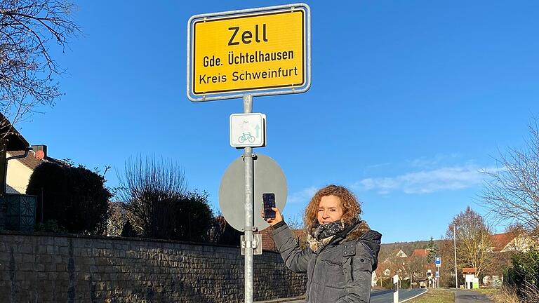 Ute Pawlik sucht mit ihrem Handy am Ortseingang von Zell im Landkreis Schweinfurt nach Empfang. Im ganzen Ort haben Kunden der Telekom keinen oder nur schlechten Empfang.